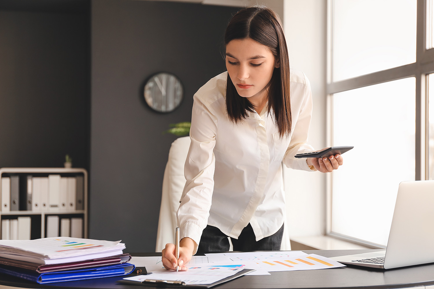 woman in white shirt standing over work desk writing on a document