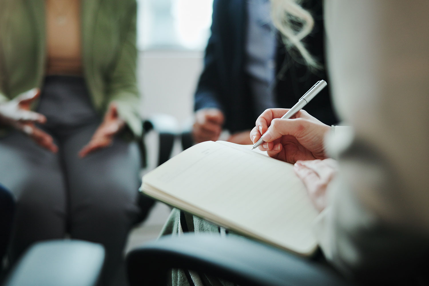 person writing on clipboard with 2 people talking in background