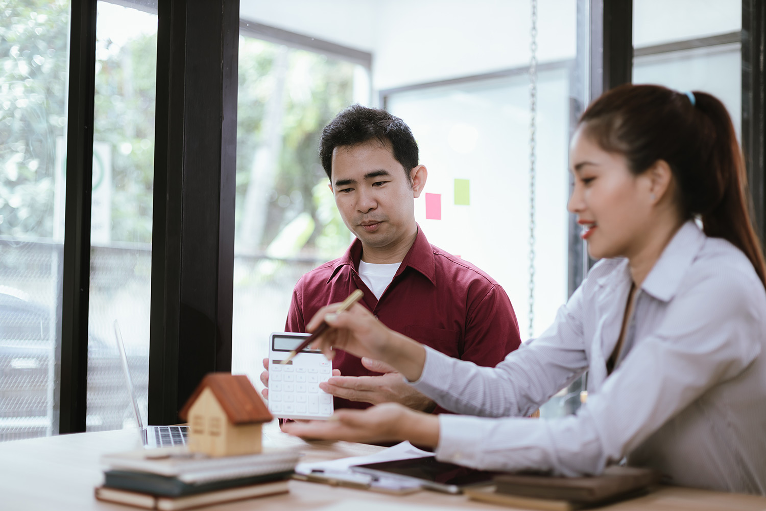 man and woman sat at a desk, with woman offering property accountancy advice. A stack of books with a model house on top rest on the table