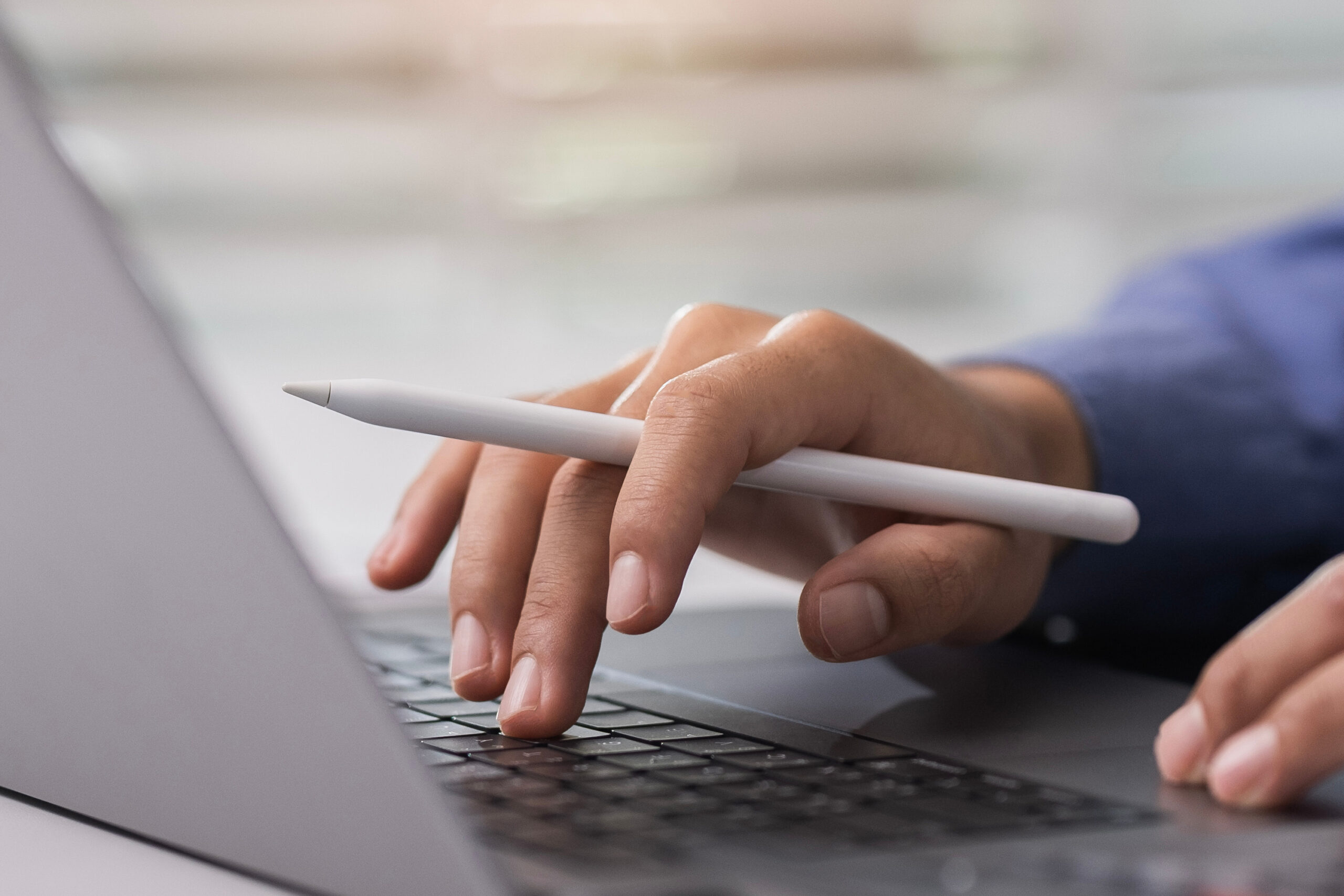Hand holding a pen, one typing on laptop, the other typing on a calculator.