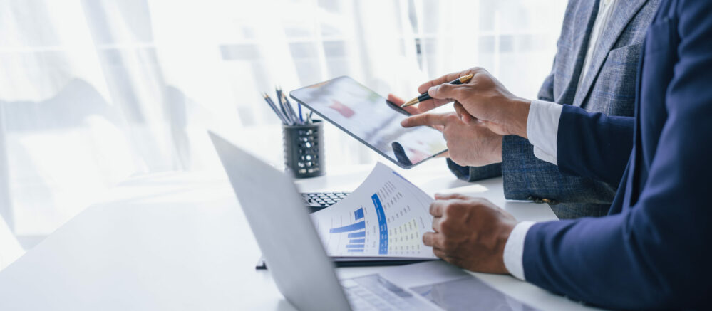 Person in suit, on tablet sitting at desk with his laptop and graphs